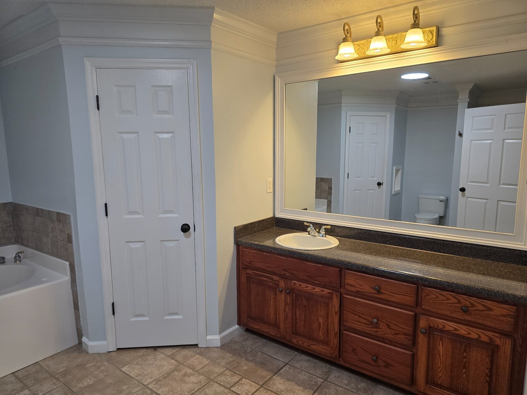 Bathroom vanity with wood cabinetry, stone-look counter, and large mirror